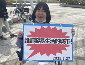 自立生活センターほにゃらで中国語で書かれたパネルを持ってアドボカシー活動をする笑顔のココさん